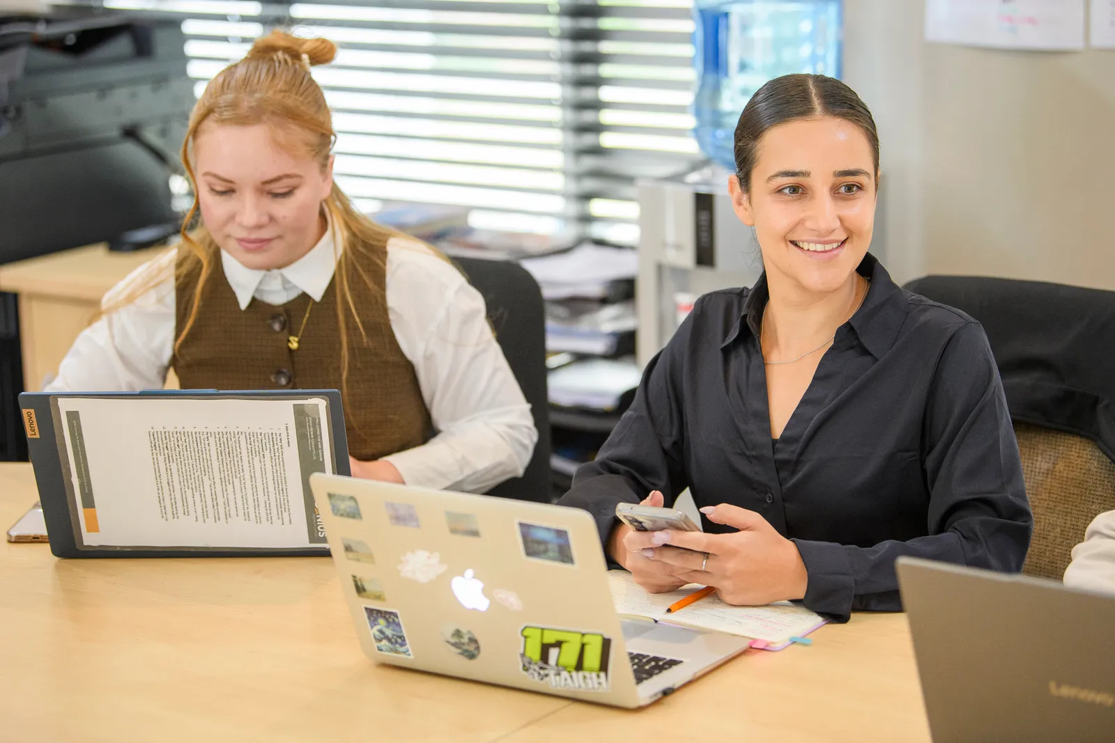 A Genius team member smiling beside a colleague working with a notebook