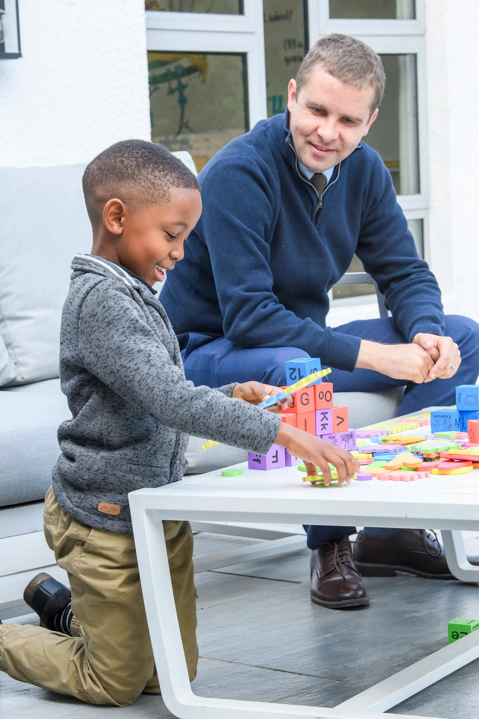 A tutor watching a young learner build with colourful alphabet blocks